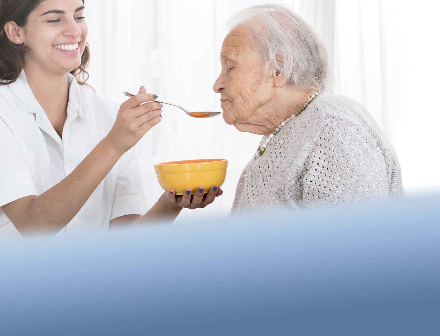 Pflegerin füttert pflegebedürftige Seniorin