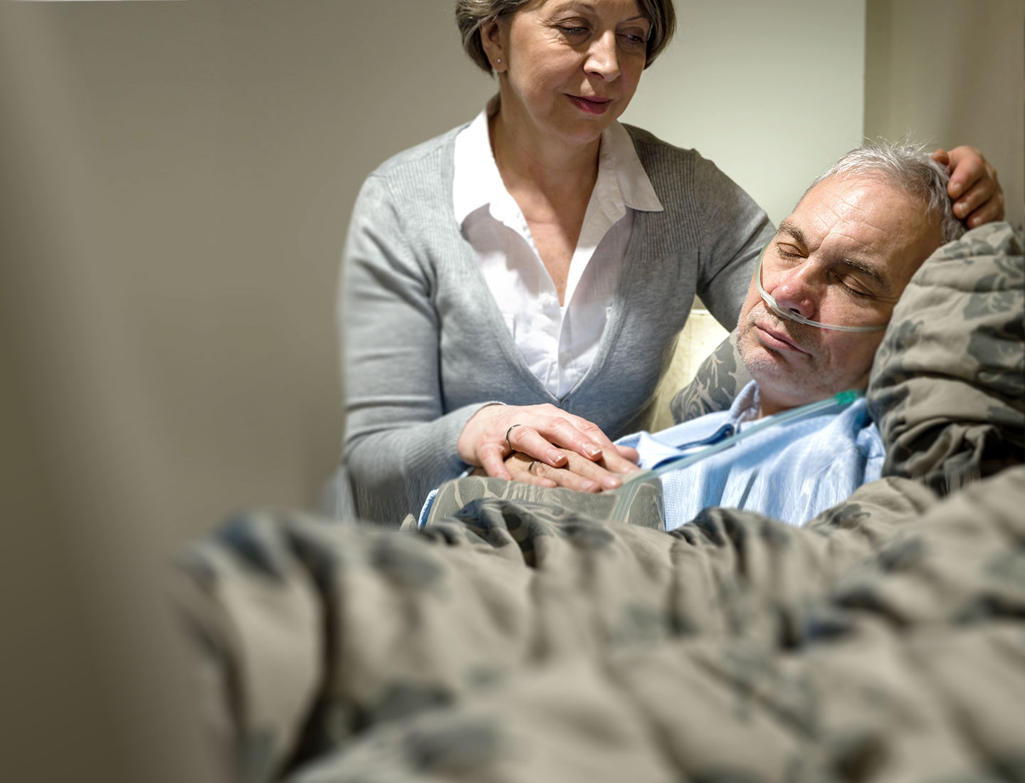 Mann in Krankenbett wird von Frau umsorgt