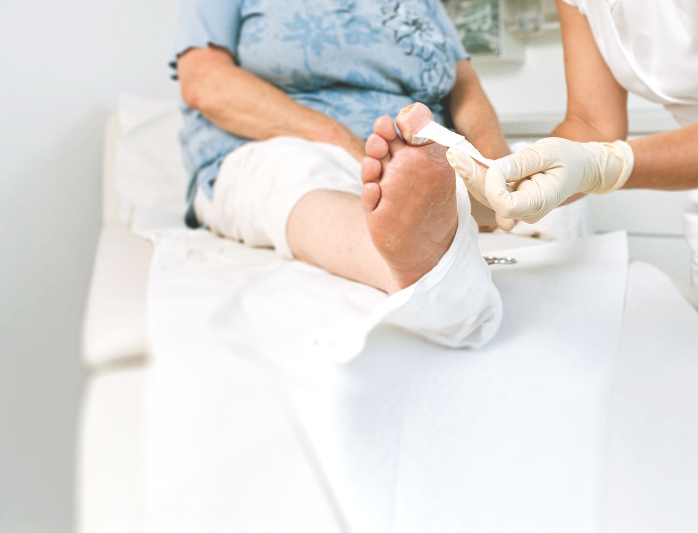 Arzthelferin versorgt Wunde am Fuß einer Seniorin