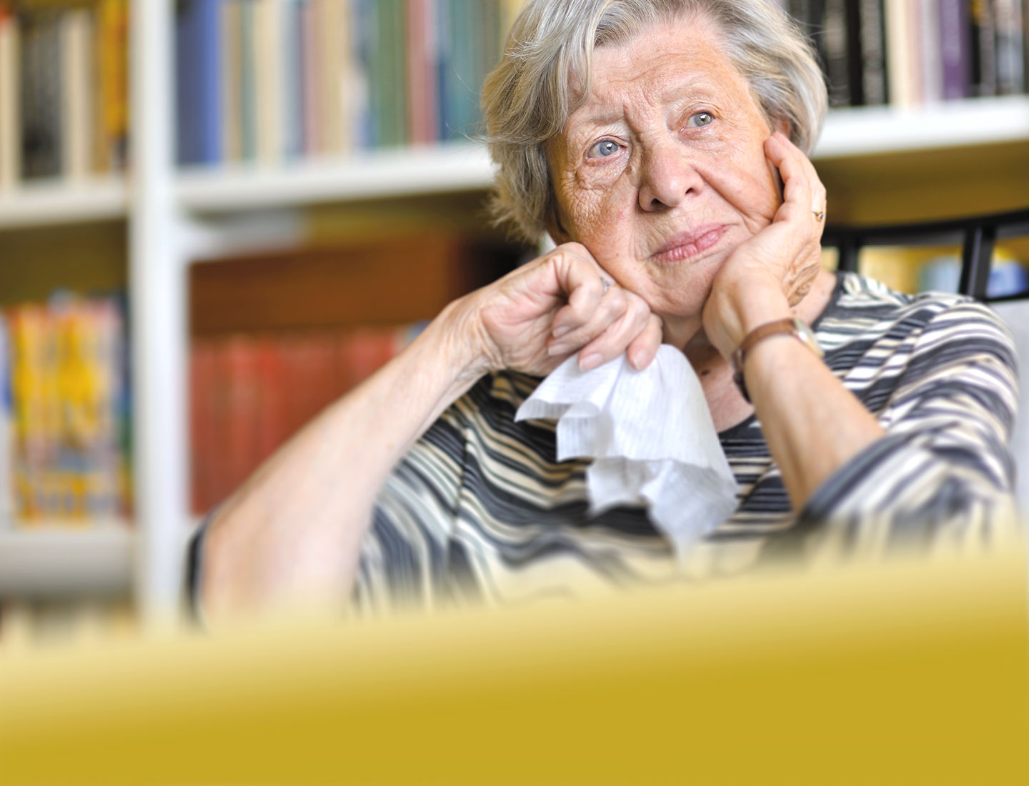 Seniorin sitzt nachdenklich an Tisch mit Taschentuch