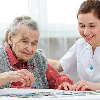 Pflegerin mit Seniorin beim Puzzeln