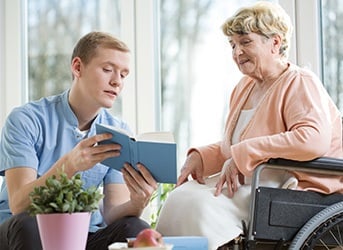 Pfleger liest Frau in Rollstuhl aus einem Buch vor