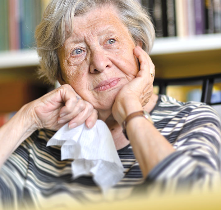 Seniorin sitzt nachdenklich an Tisch mit Taschentuch