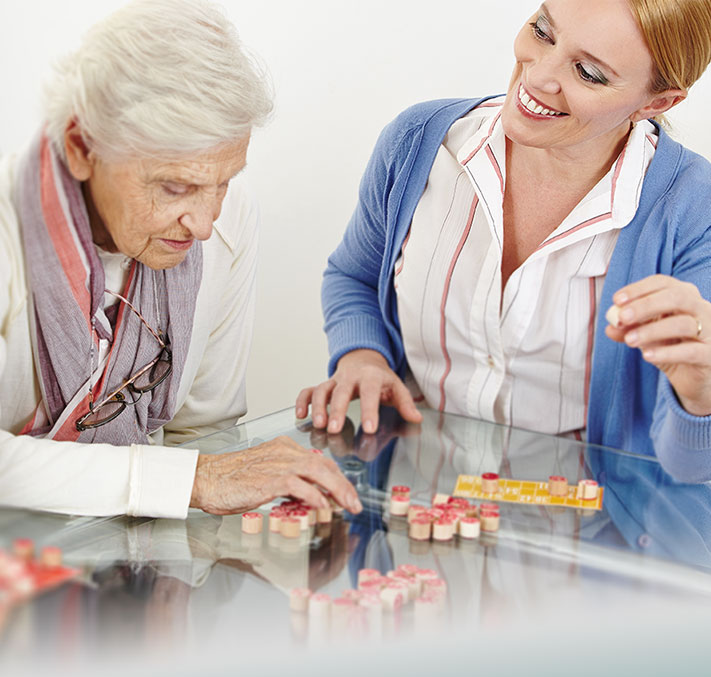 Pflegeperson macht Brettspiel mit Seniorin