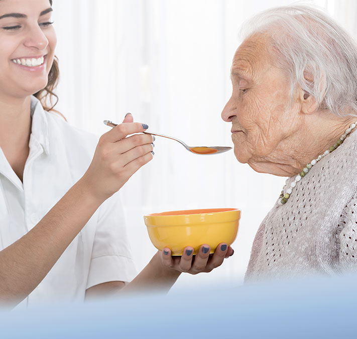 Pflegerin füttert pflegebedürftige Seniorin