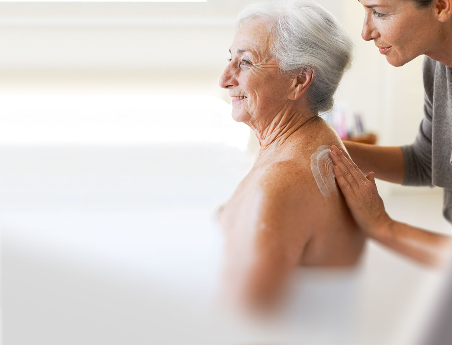 Pflegeperson cremt einer pflegebedürftigen Seniorin die Haut ein