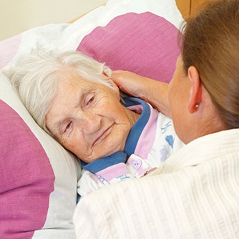 Ältere Dame wird von Pflegerin im Bett zurecht gelegt
