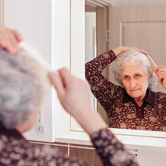 Ältere Dame kämmt ihre Haare vor dem Spiegel