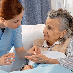 Pflegerin verabreicht einer pflegebedürftigen Seniorin ihre Medikamente