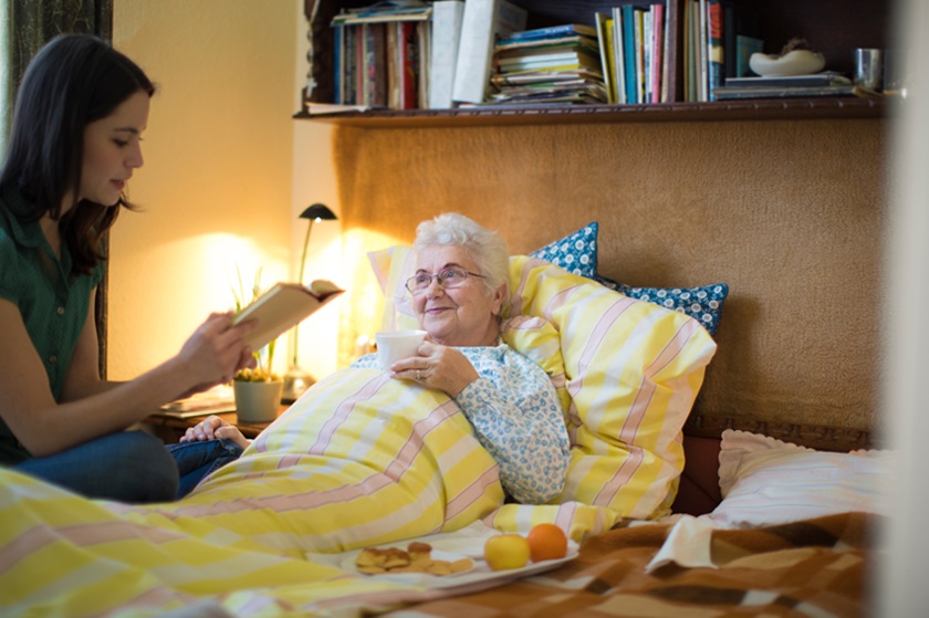 Frau liest pflegebedürftigter Seniorin etwas vor