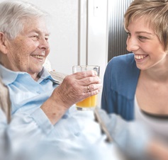 Seniorin trinkt Orangensaft mit Pflegeperson