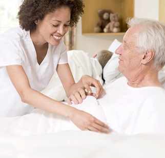 Senior wird von Pflegeperson im Bett zugedeckt
