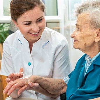 Pflegerin cremt pflegebedürftiger Seniorin die Haut an den Händen ein