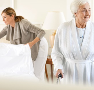 Pflegeperson macht das Bett einer pflegebedürftigen Seniorin