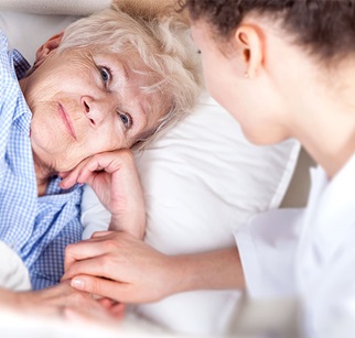 Pflegerin sitzt bei dankbarer Seniorin am Bett